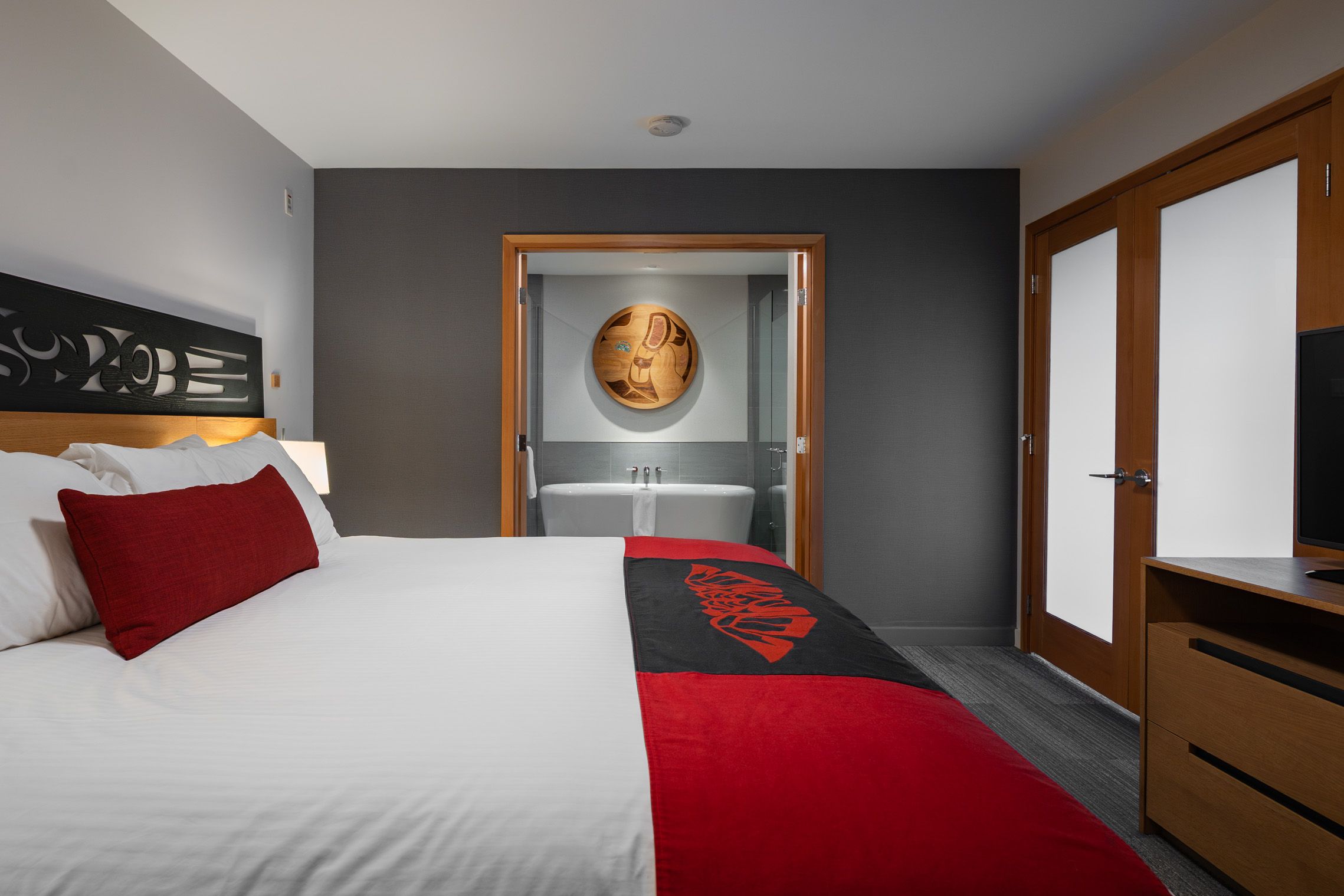 large and comfortable hotel room at Kwa'lilas Hotel in Port Hardy, BC. The room features Indigenous art and carvings, a TV and a free standing bathtub.