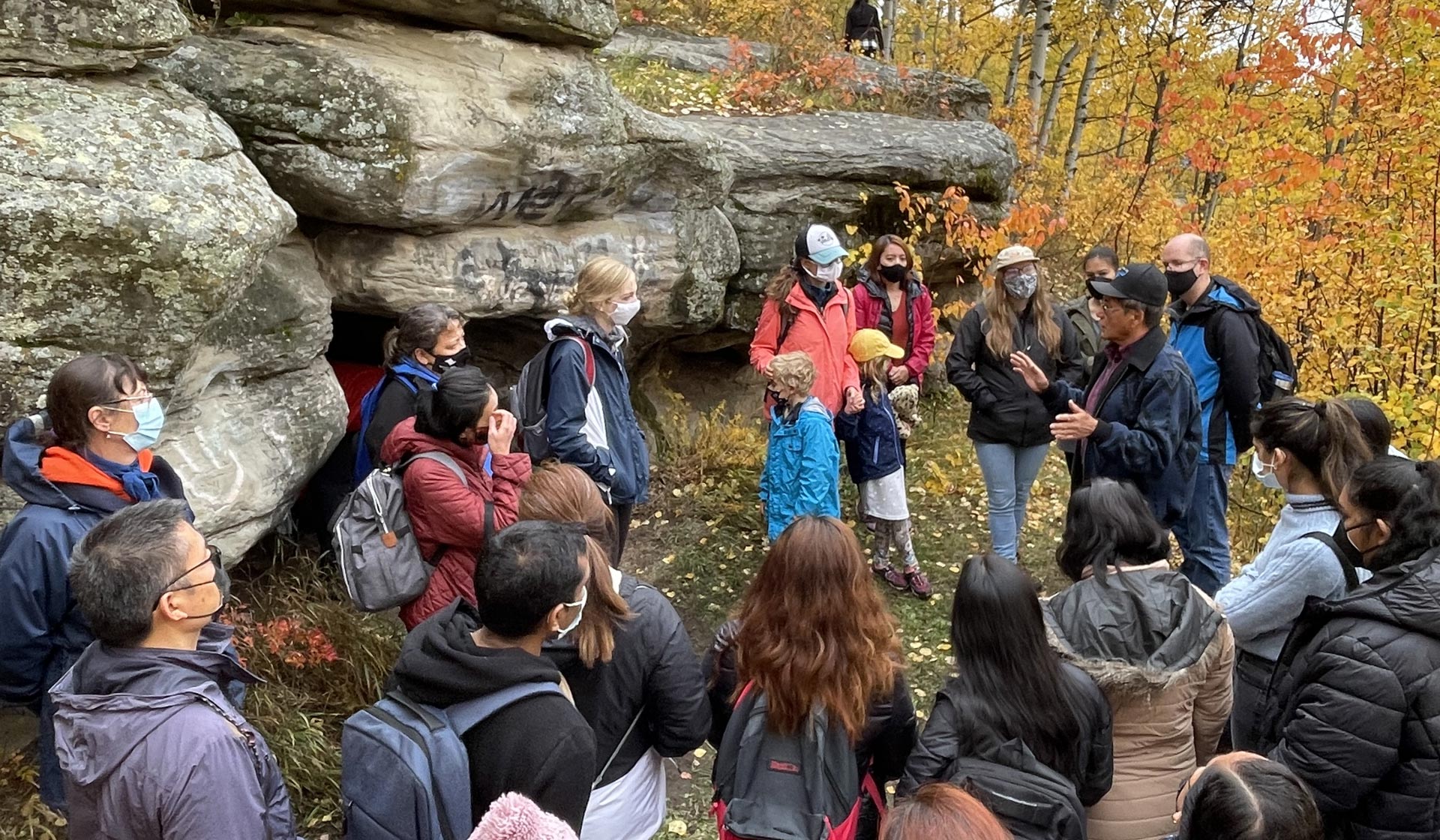 Group tour at Tse'k'wa National Historic Site at Charlie Lake- guests in front of cave learning from local guide at the sacred site