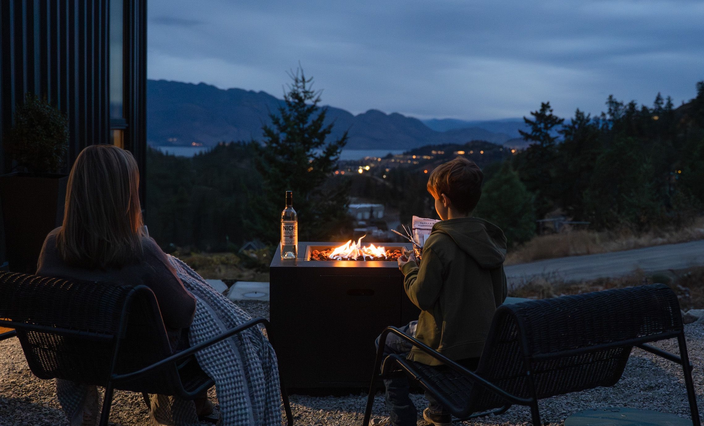 A mom and son at Niche Wine Co. enjoying the cozy night and mountain view of West Kelowna by the fire.