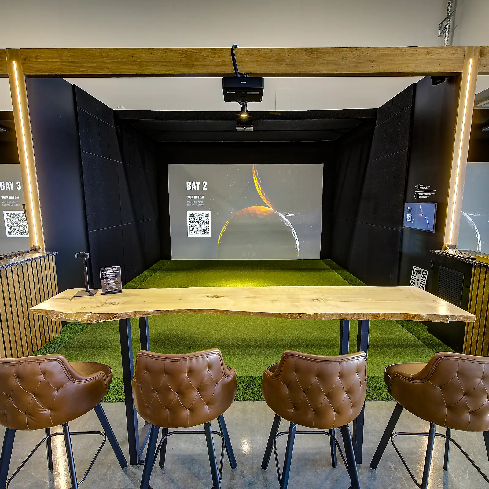golf bay at indoor golf simulator facility in Westbank, with beautiful live edge wooden bar, turf for golfing on and a large screen to shoot at