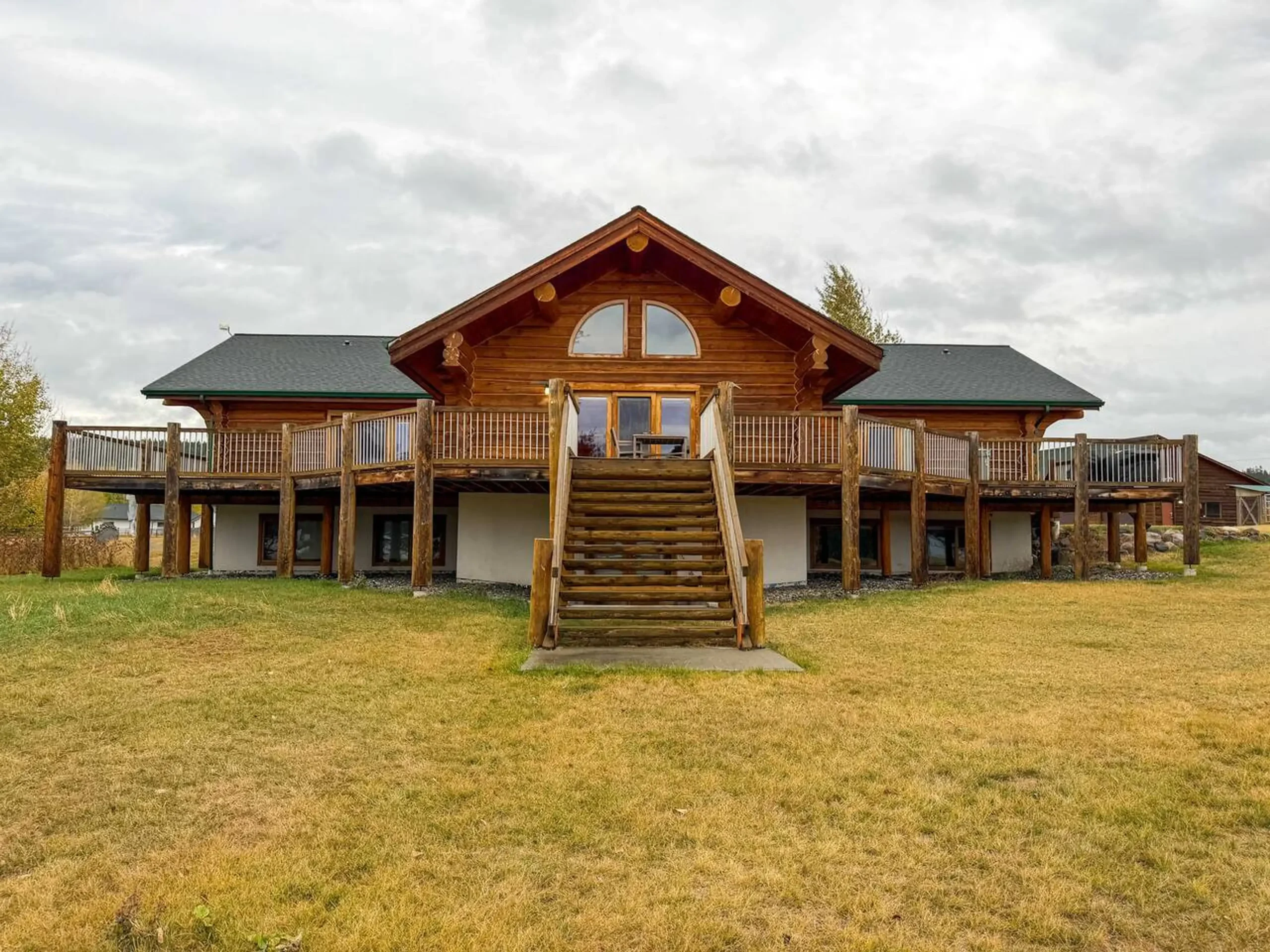 Cpluk'wten (Gathering Place) in Lac la Hache, Eagles Nest, 18 guest cabin situated on green lawn with cloudy skies.