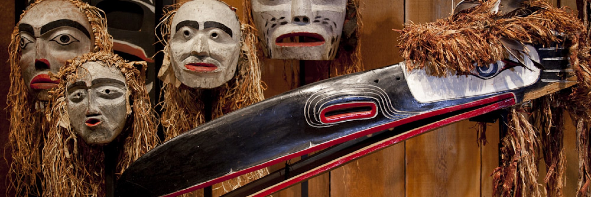 A collection of Indigenous masks hung on a wooden wall