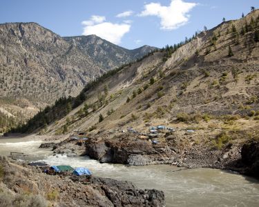Tents are pitched on both sides of a river at the bottom of hill in Lillooet, BC.