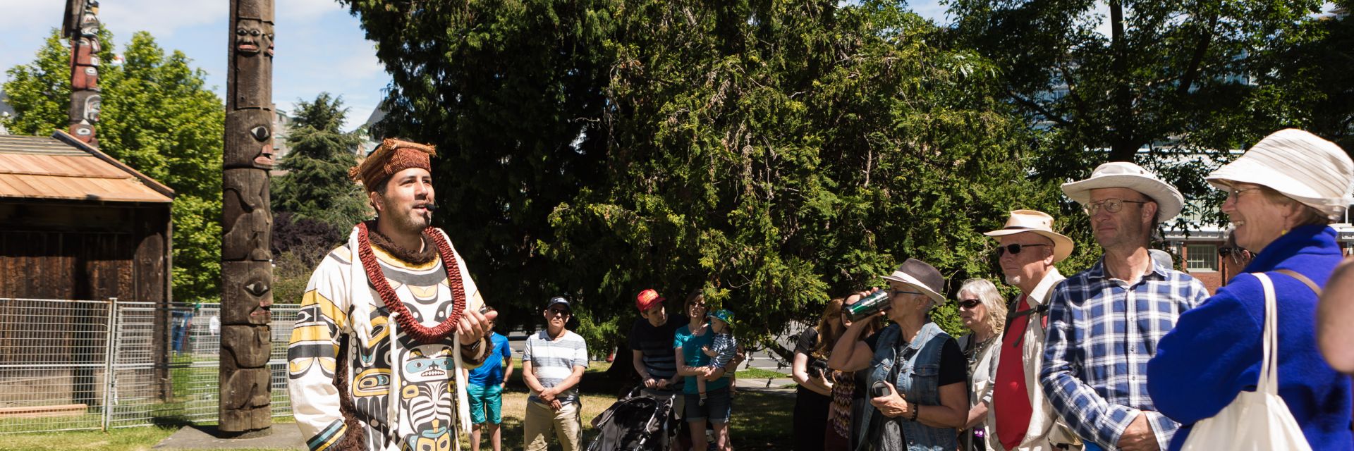 A man wearing traditional Indigenous clothing speaks to a crowd