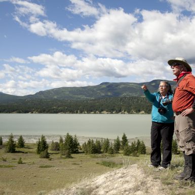 A woman and man stand together on a sandy hilltop next to a lake