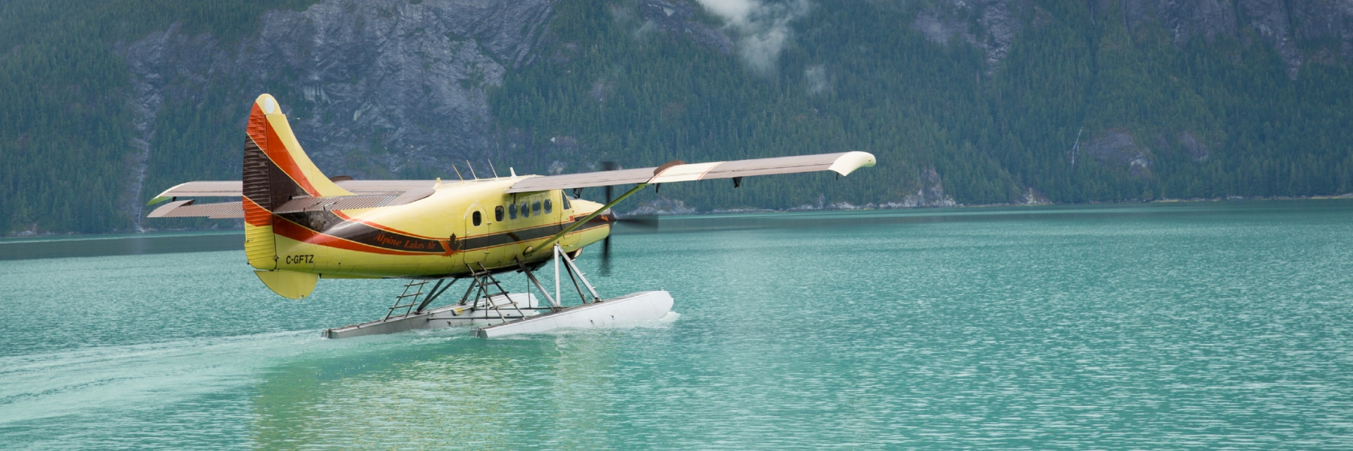 A yellow and red sea plane sitting in a bright blue lake