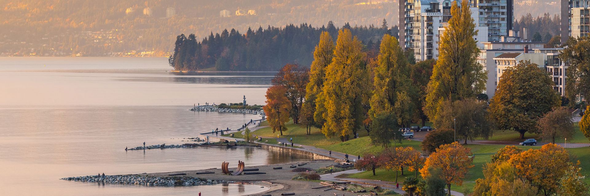 A landscape view of a shoreline with a walking path, trees and white buildings