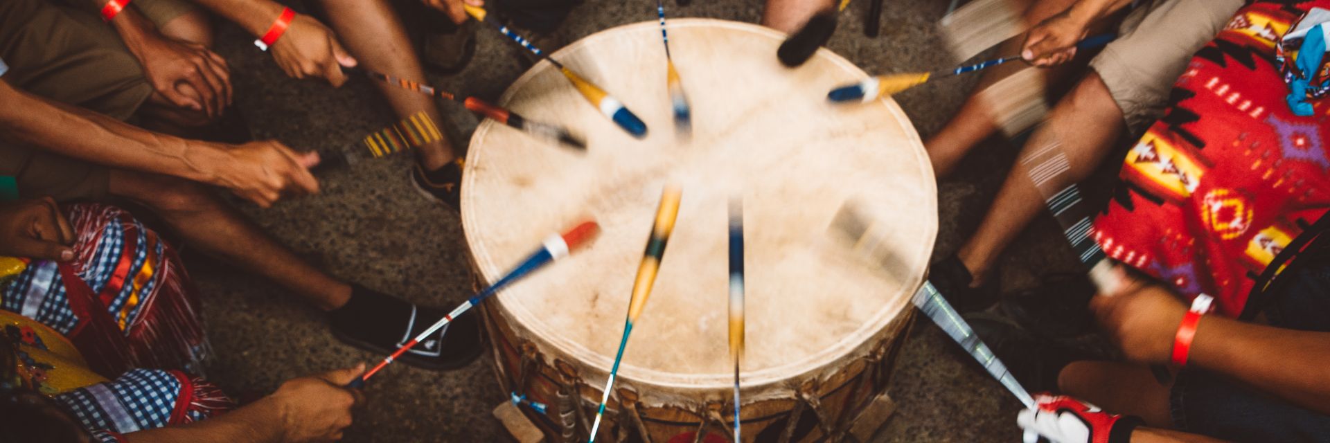 A group of people play a Indigenous drum together in a small circle