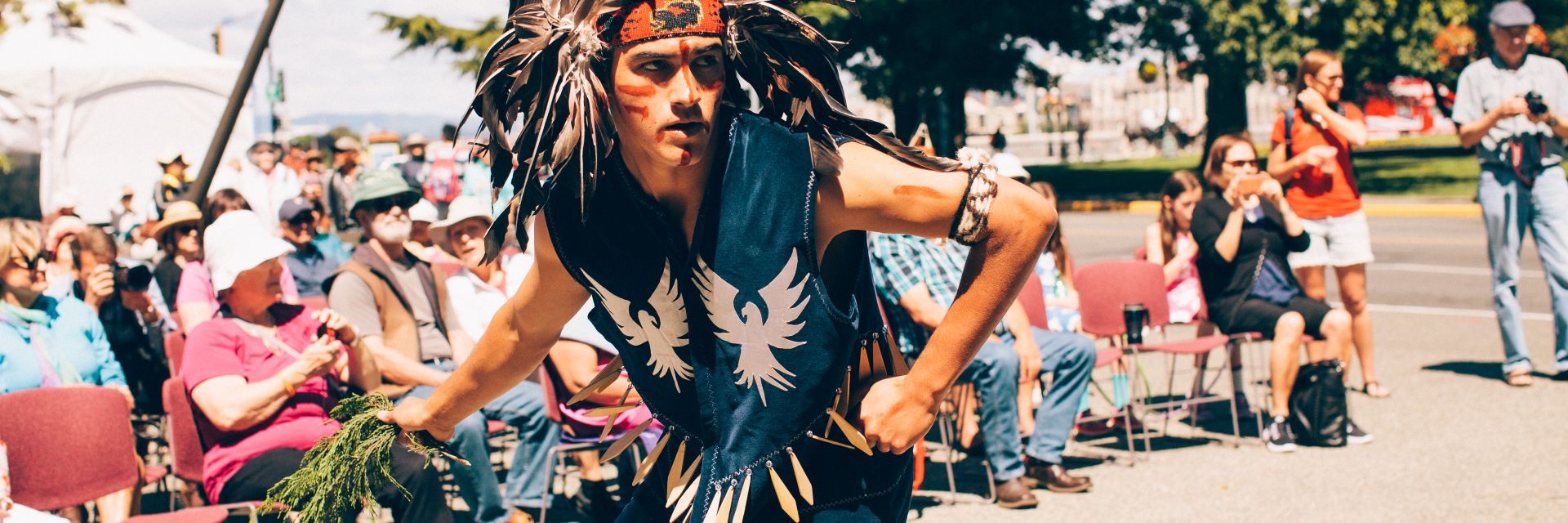 A man wearing traditional Indigenous clothing strikes a pose in front of a crowd